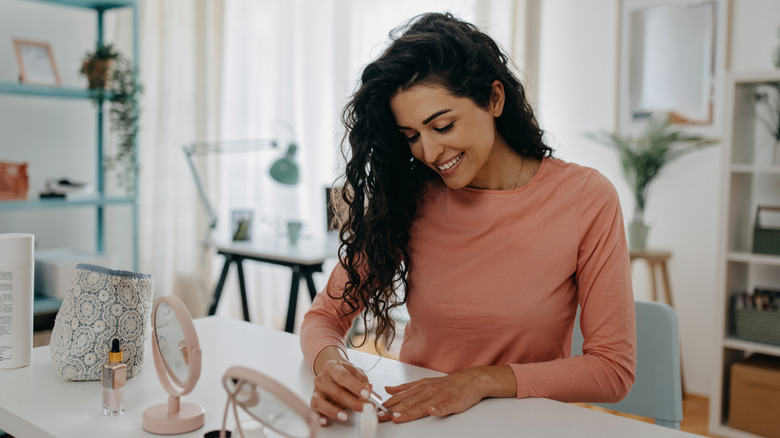 Smiling, curly-haired woman doing an at-home manicure at her desk