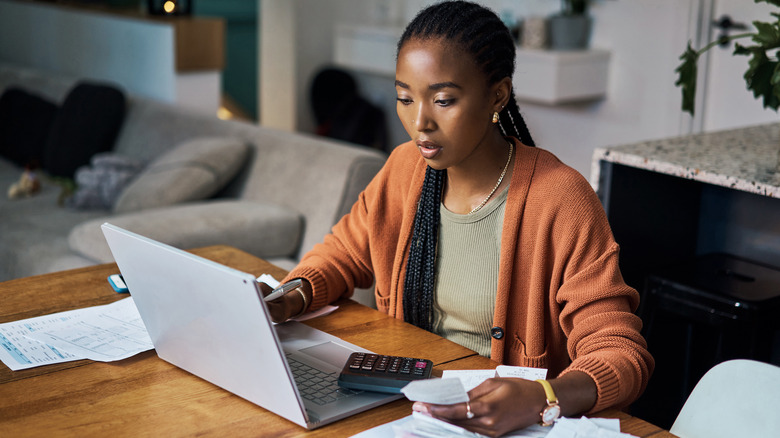 Woman looks at laptop with paperwork