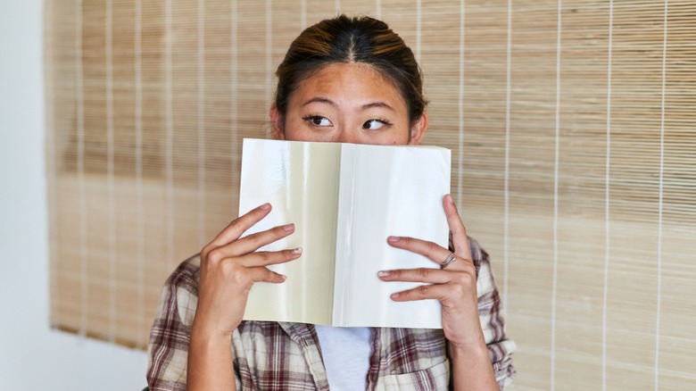 A woman holding an open book in front of her nose and mouth
