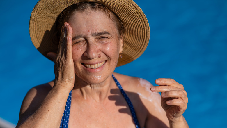 Mature woman with long gray hair applying cream to her cheek