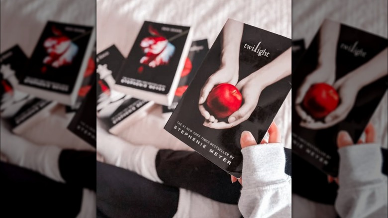Someone sitting on a bed holding a copy "Twilight" with the rest of the series spread out in front of her