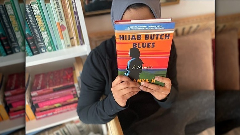 Lamya H covering her face with book