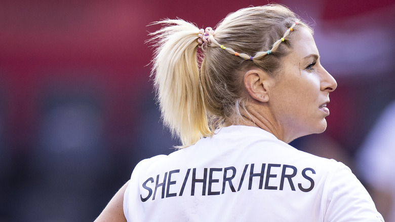 A woman wearing a she/her top, looking away