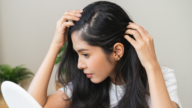 A woman examines her scalp and hair in a small mirror