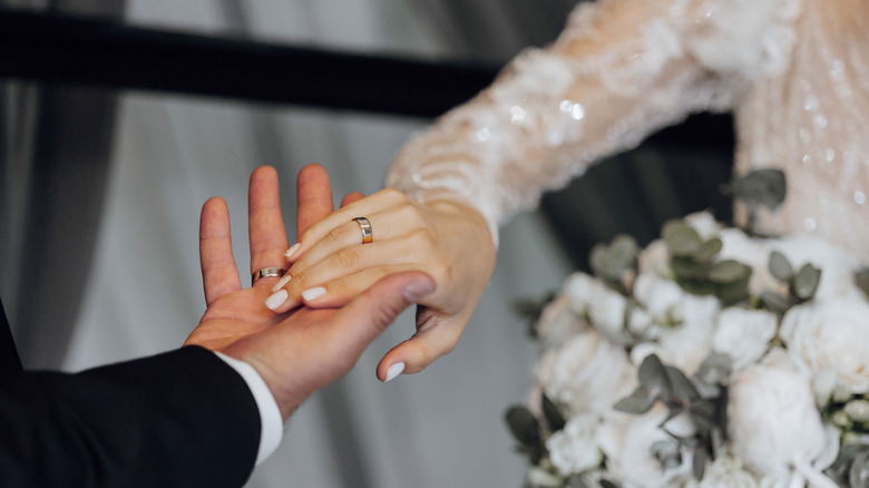 A bride holding the groom's hand with a bouquet of flowers in the background