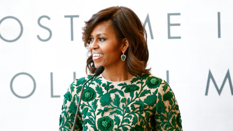 Michelle Obama in a green accented dress and speaking at a podium
