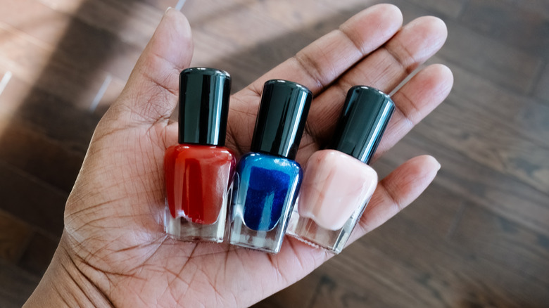 A close-up of a person's hand carrying three nail polish bottles