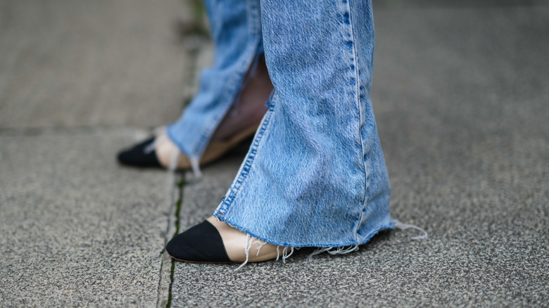 Model standing in flared jeans and white open-toe heels