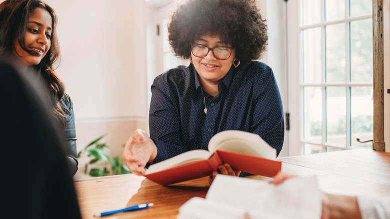 A woman looking at an open hardback book sitting at a table