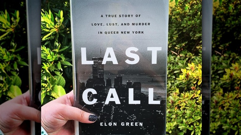 Hand holding book in front of greenery