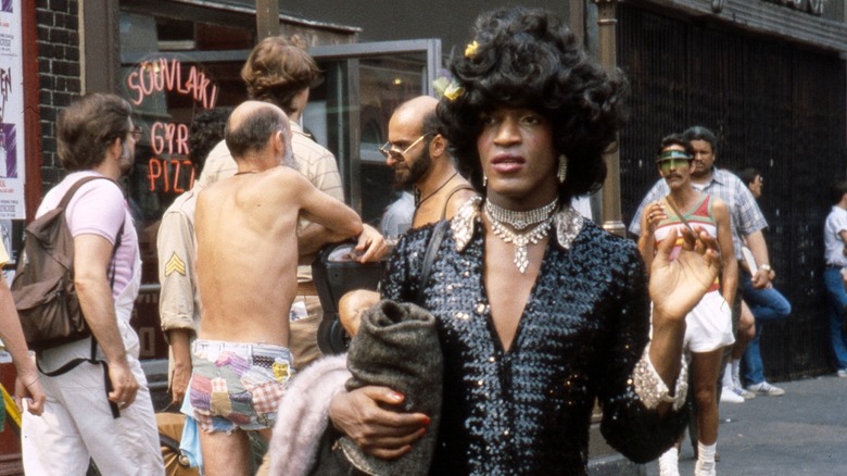 Marsha P. Johnson walking on a busy street in a black dress