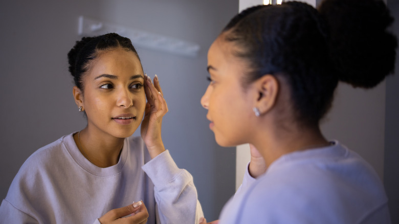 Woman looks at skin in mirror