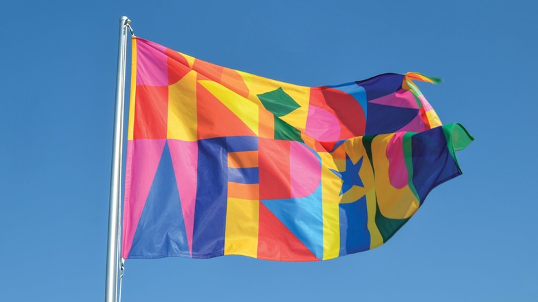 Colorful flag on a flag pole billows in the wind against a blue sky
