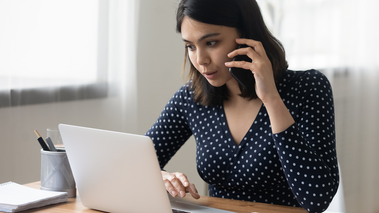 Woman on phone while looking at her laptop screen